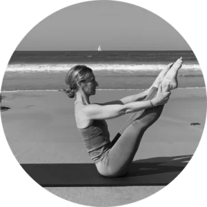 Portrait en noir et blanc de Véronique Bozier, professeure de Pilates, effectuant une posture de Pilates sur une plage avec l'océan en arrière-plan.